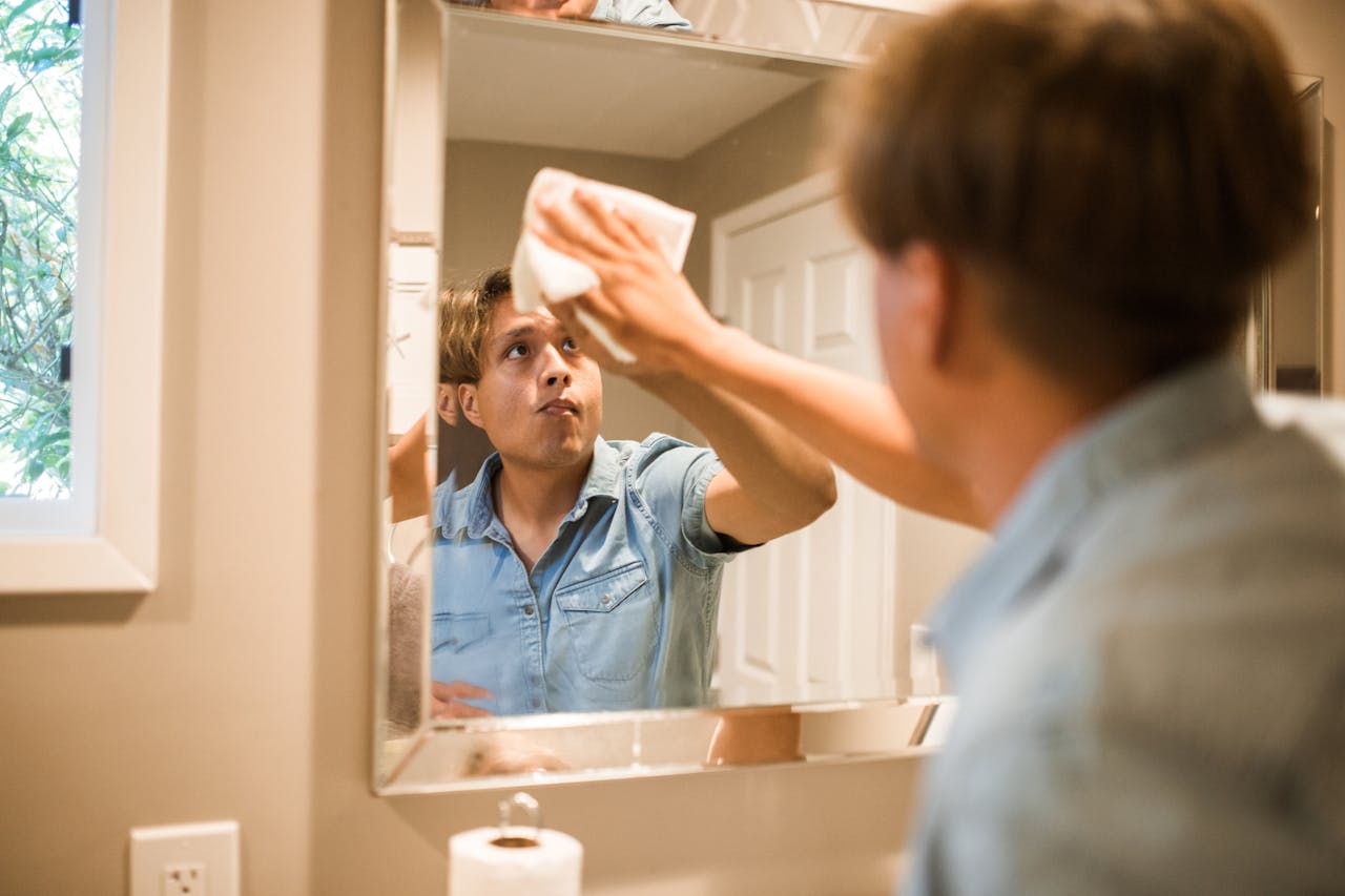 A man wiping a bathroom mirror, focusing on cleanliness and hygiene in a domestic setting.